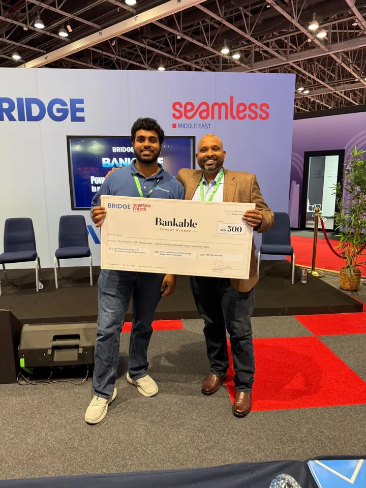 Jaya Sriram Ganeshna and Sridhar Kotari holding a BANKABLE Cohort Winner presentation cheque beside Bridge and Seamless signage